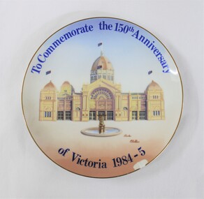 Circular ceramic plate commemorating the 150th anniversary of Victoria in 1984-85, depicting a painting of the Royal Exhibition Building in Melbourne and signed by the artist Charles Mc Cubbin.