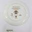Back of a ceramic plate commemorating the 150th anniversary of Victoria, with an inscription about the plate and the artist's signature, as well as the plate number 0404 and three trade marks. Black and white 5 cm scale in the foreground.