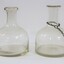 Side view of two clear glass water containers/bottles, one with a metal chain around the narrow neck. 