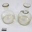 Two clear glass water containers/bottles, one with a metal chain around the narrow neck.  Black and white 5 cm scale in the foreground.