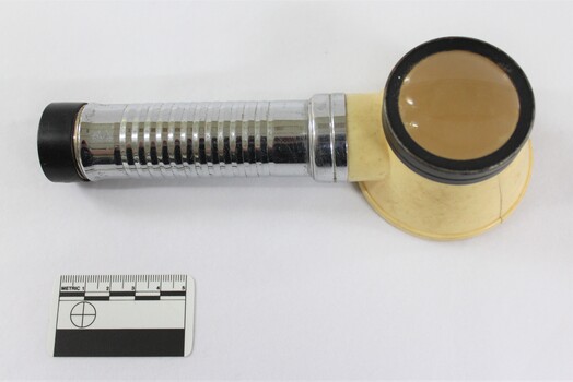 Metal and plastic flashlight magnifying glass from above, with a black and white 5 cm scale in the foreground. 