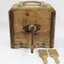 A large wooden box with metal turning handle on the face, with two butter paddles
