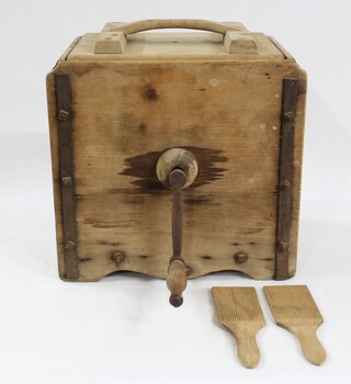 A large wooden box with metal turning handle on the face, with two butter paddles