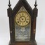A gothic style wooden clock with gold and white embellishments, and Roman Numeral numbering on the clock face