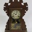 An ornate wooden clock with Roman numeral clock face and glass door with a decorative gold transfer. 