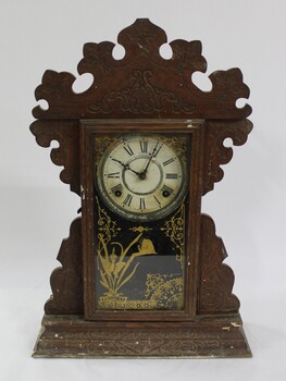 An ornate wooden clock with Roman numeral clock face and glass door with a decorative gold transfer. 
