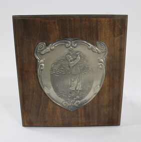 A wooden plaque with a metal engraving depicting a male golfer