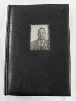 A black photographic album with a photograph of a man inserted into the front cover