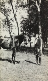 A black and white photograph of a woman with a horse in the bush printed as a postcard