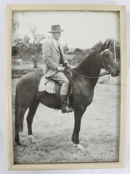 A black and white photograph of a man sitting atop a horse