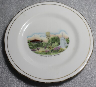 A white plate with gold trim. A hand painted image depicting Woodland Grove, Wodonga is in the centre.