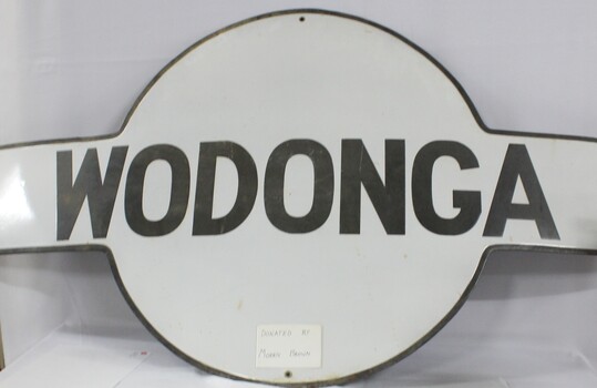 A railway station sign from the Wodonga station. Wodonga in black on a white background.
