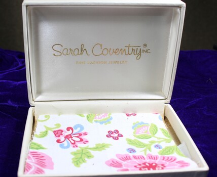 Inside of jewellery box, white with floral paper lining. Sarah Coventry company logo on inside of lid