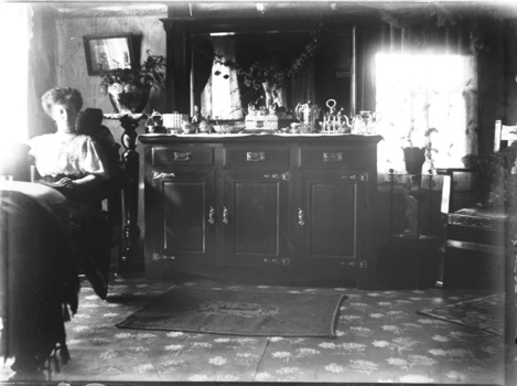 Mrs. McFarlane on the left of the image sitting beside a dressing holding silverware.