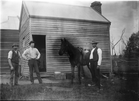 Three men and a horse beside a building