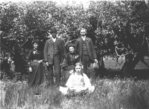 An image of five members of the Young Family including two women, two men and a young girl seated on the ground.