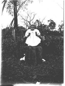 Baby in a white dress being held up for the photo. Person in background is hidden from view.