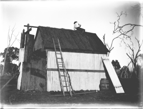 A house under the final stages of construction. A ladder leans against the wall and a man is working on the roof.