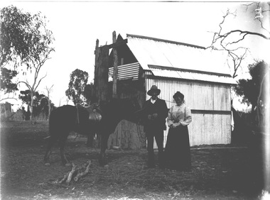Mr. and Mrs. Egan standing in front of a house with a saddled horse. 