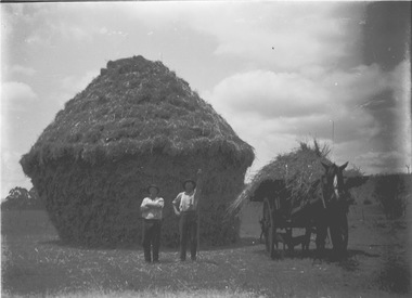 Two men in front of a haystack. A horse and cart loaded with hay are on the right.