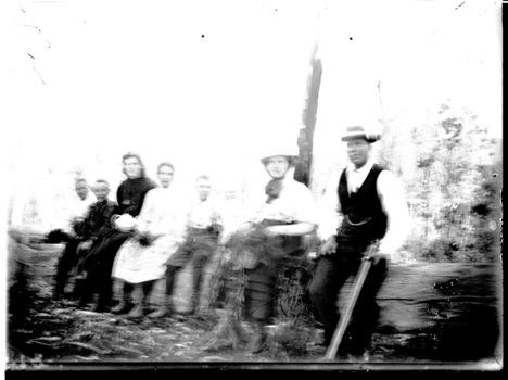 A group of seven people sitting on a log.