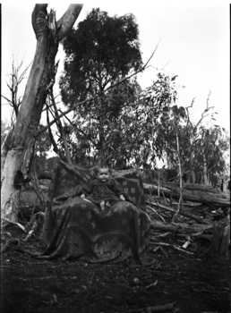 A baby is seated on a chair in the centre of the image.  The chair is covered by a blanket.