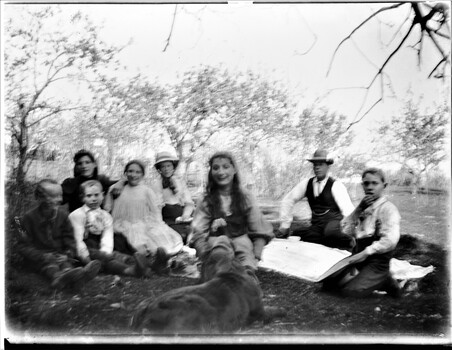 A family group sitting outside having a picnic. There are trees in the background.