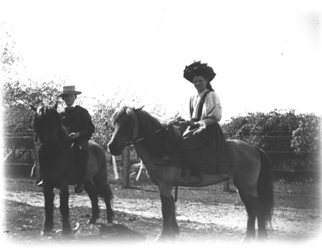 Boy and girl astride their ponies. The girl is seated side-saddle.