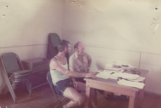 David Naldrett and Rex McDonnell  seated at a desk covered with paperwork.