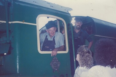 Driver Len Gregson leaning out of the Locomotive. Fireman in the background and 2 women on platform