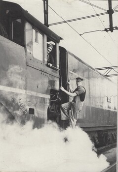 Driver Tom Black in cab of locomotive and Fireman Hec Lloyd climbing up ladder.