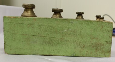 Side view of metric weights in a green wooden holder