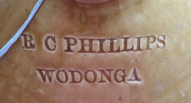 Business name of "R C Phillips" inscribed into top of ceramic demijohn in tan coloured section.