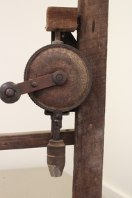 Side view of metal hand drill mounted on wooden stand