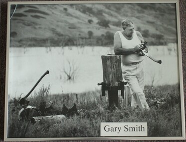 Garry Smith, a champion axeman, sharpening the blade of an axe. Another axe is on a log to the left of the image.