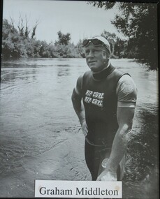 Swimmer standing at edge of Murray River wearing a wet suit and goggles.