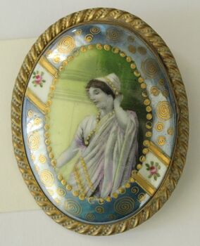 An oval brooch featuring an image of a Grecian style woman in profile