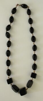 A string of black beads of various sizes with metal hook clasp.
