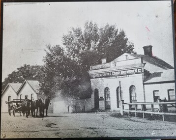 Black and white photo of brewery buildings. A horse drawn cart is in the left foreground.