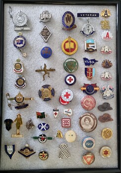 Collection of 50 varied badges representing a range of organisations mounted in a frame 