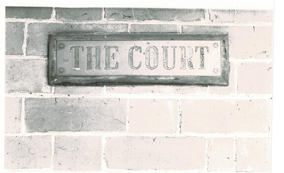 Copper court sign on wooden base attached to the brick wall of the court house