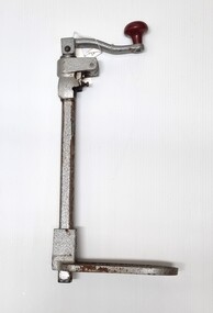 Large iron can opener with red knob on handle