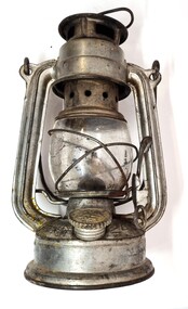 Small metal and glass kerosene lantern showing screw top to open fuel container base.