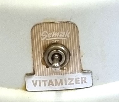 Semak logo surrounding the power control on front of base.