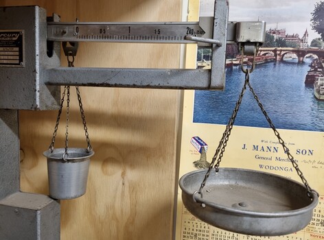 Arm of scales with tray, J, Mann & Son calendar in background