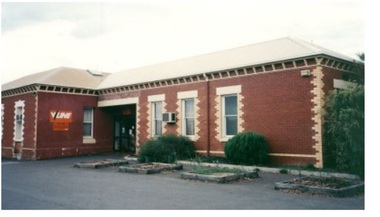 A red brick building with white window casements. V/Line sign near the door