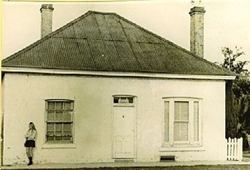 Old stone building with tin roof. Person leaning against the wall at left.