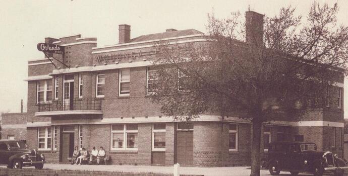 A large brick building with people sitting on a bench at the front.
