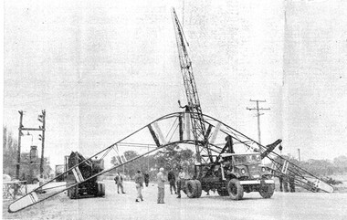 Construction workers with a large iron boomerang attached to a crane,