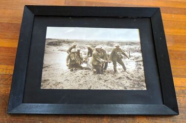Photo, Photo of seven diggers transporting a wounded digger thru the mud on the Somme in 1917. Note burial cross in background, 1917